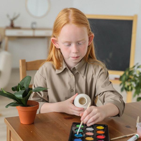 A girl with long light red hair painting with watercolors. 