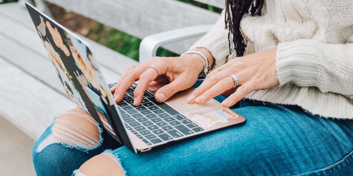 Torso and lap of a person in torn blue jeans typing in a laptop.