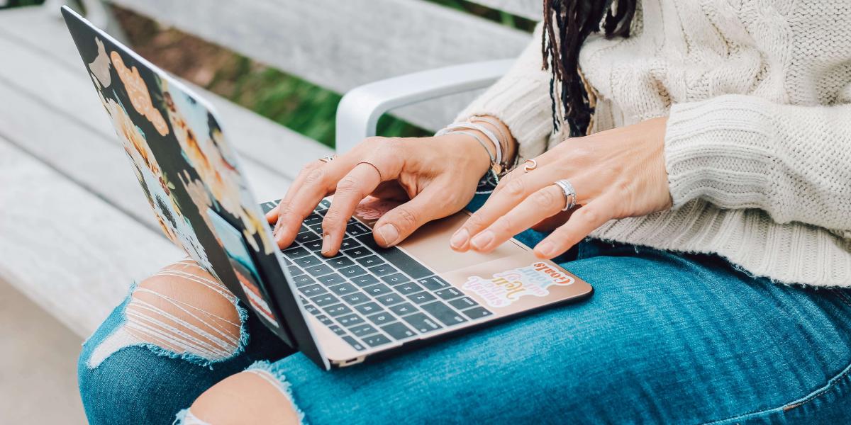 Torso and lap of a person in torn blue jeans typing in a laptop. 