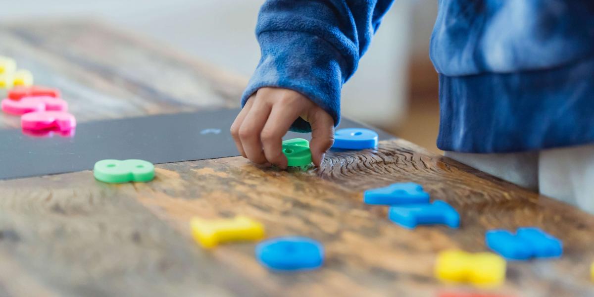 A child's hands manipulating colorful plastic letters and numbers