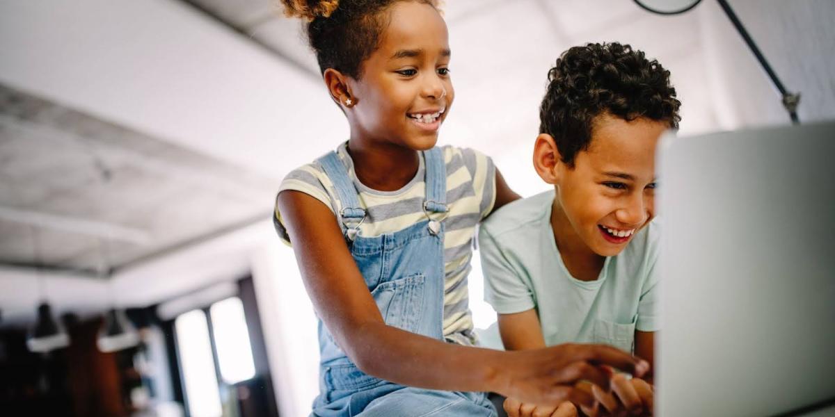 two elementary-aged children looking at a laptop and smiling